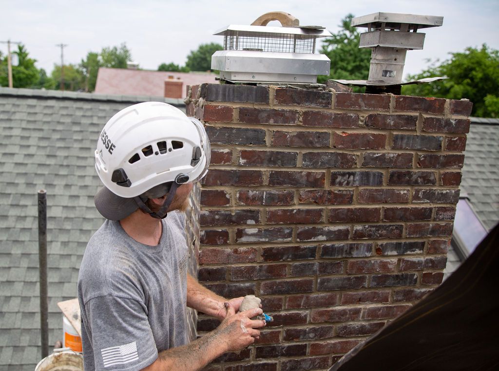 Tech with logo shirt and safety equipment repairing chimney with two chimney caps