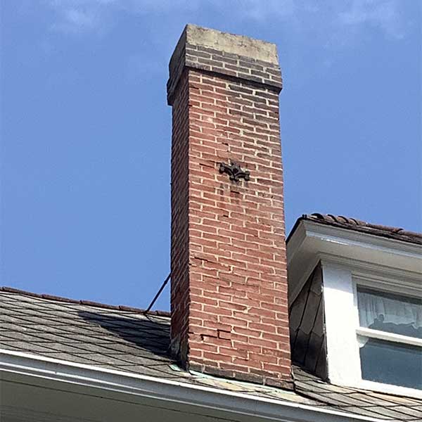 Chimney before rebuild spalling on tall chimney with wht appears to be a cross with a window to the right.