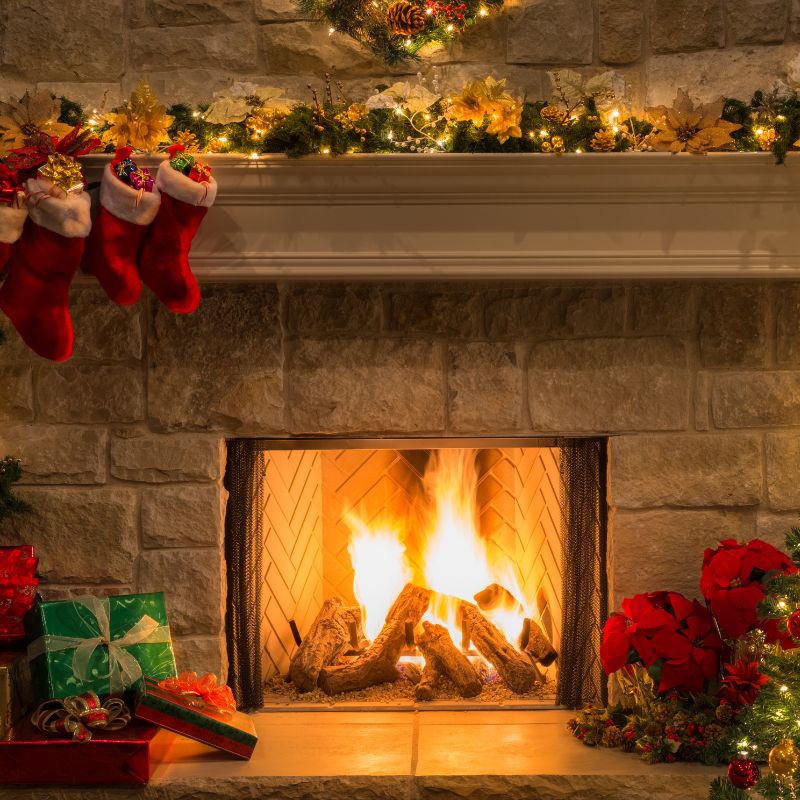 a fireplace fire burning in a stone fireplace with christmas decor around it