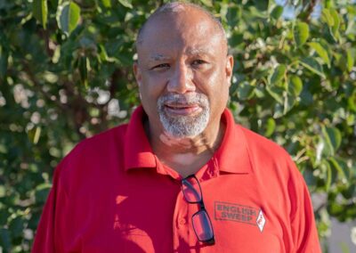Glenn - General Manager - He has a nice tan, a gray goatee and mustache. He is wearing a red English Sweep shirt with greenery in the background.