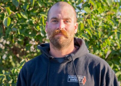 Jacob F. - Project Coach has a shaved head with a long red mustache with a short beard and blue eyes. He is wearing a hooded English Sweep pullover.
