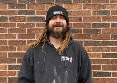 Jeremiah P. Project Coach has long auburn hair mustache and beard. He is wearing a hooded black English Sweep pullover with white mortar on his shirt (he has obviously been working. He also has on a knitted cap with a brick wall in the background.