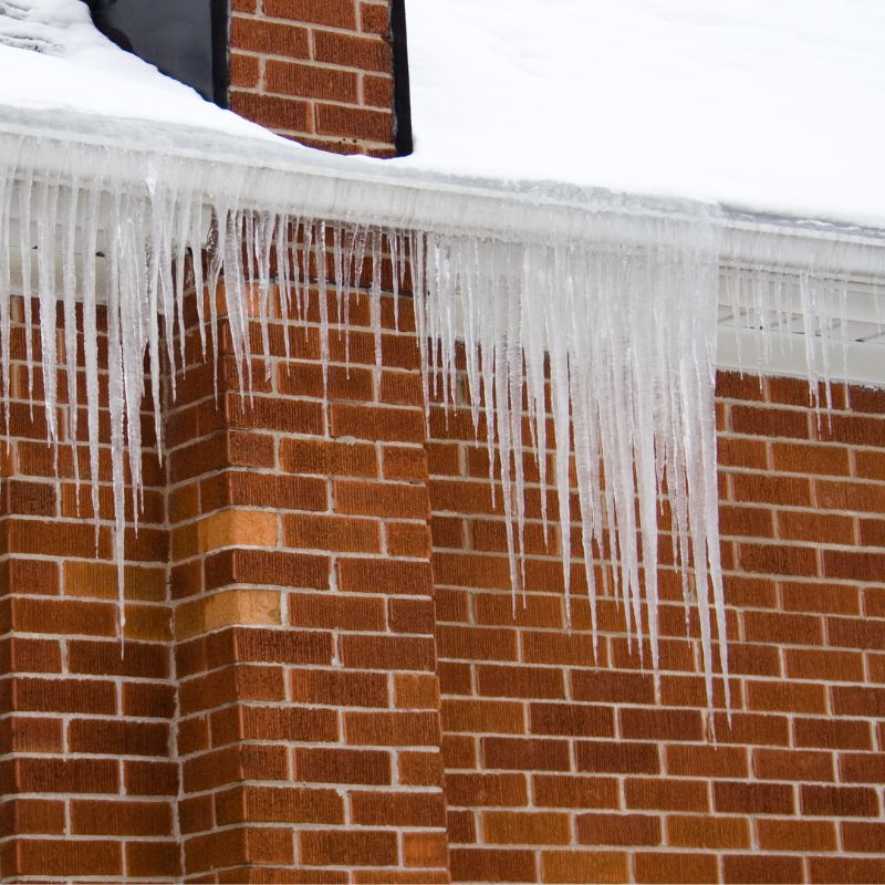 icicles hanging off of a home with masonry walls and a snowy roof